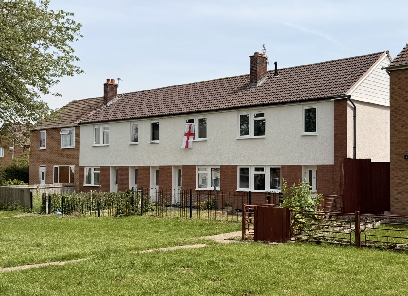 Terraced homes with rendered upper walls and tiled roofs, viewed across a grassed area.